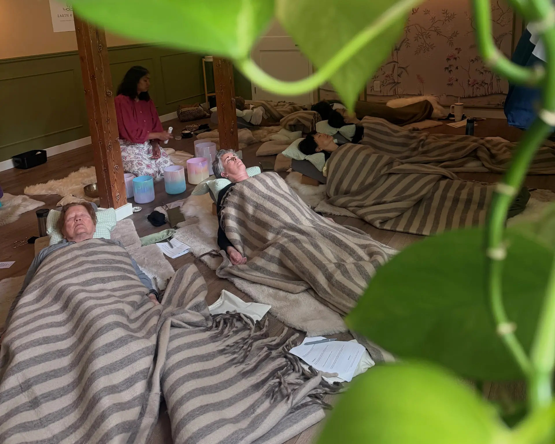 Women resting under wool blankets beside crystal singing bowls during a sound healing