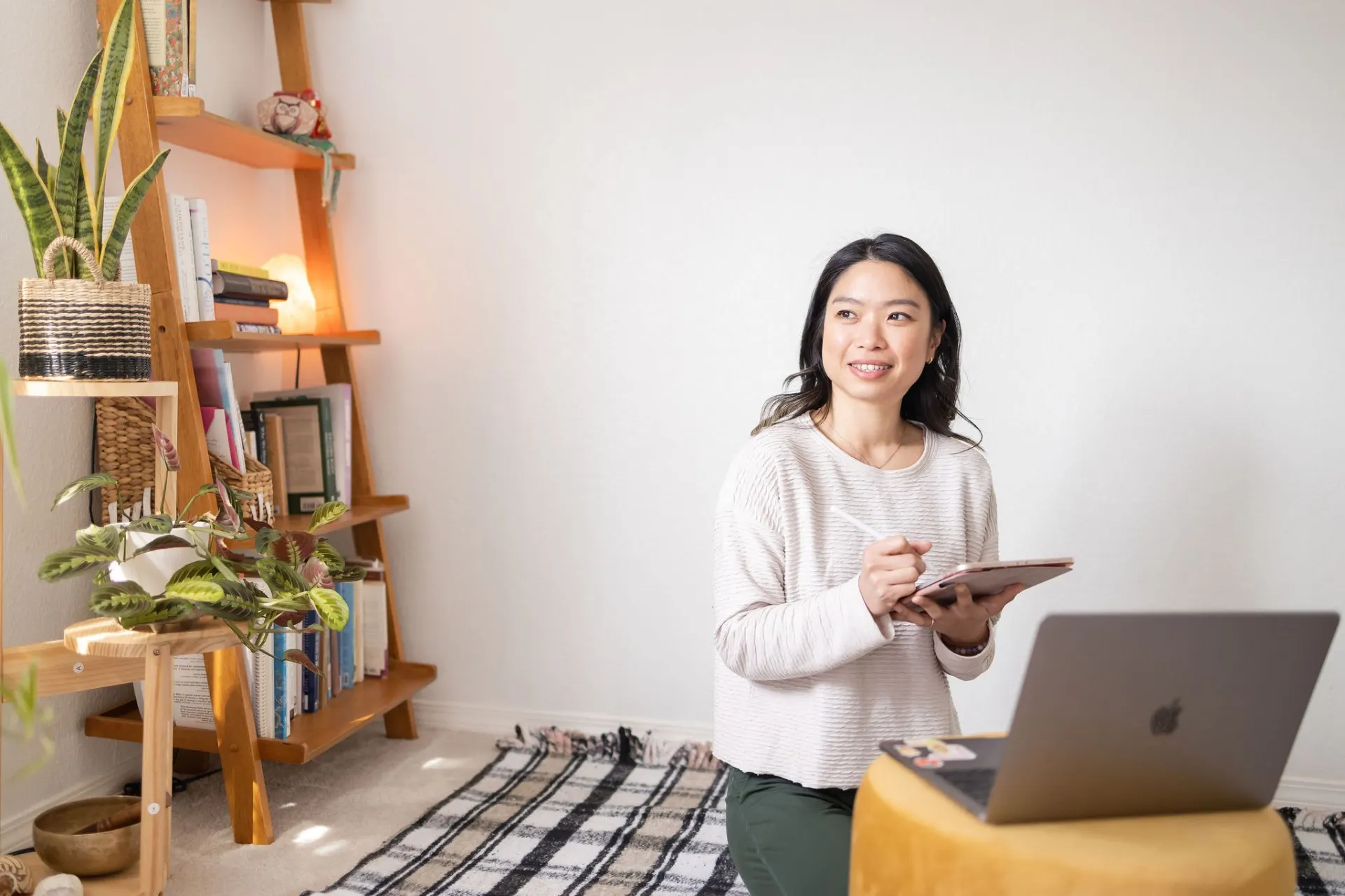 Elaine Oyang journaling in her sunlit home studio with bookshelf and plants